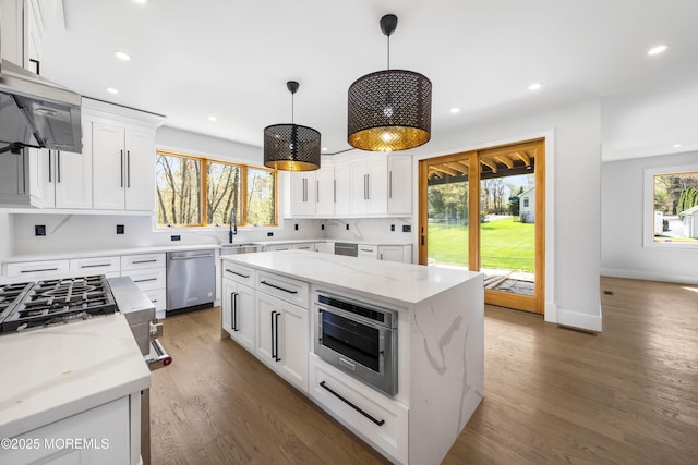 kitchen featuring recessed lighting, wood finished floors, stainless steel dishwasher, a sink, and a center island