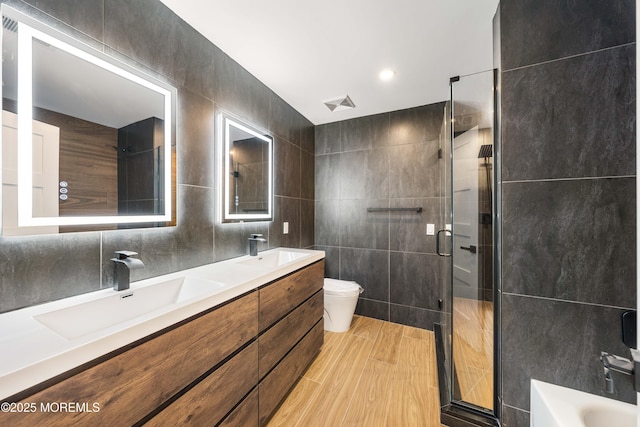 full bathroom with tile walls, a sink, a shower stall, and toilet