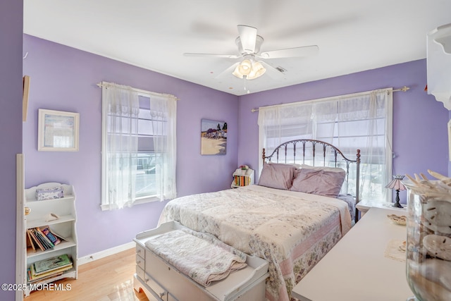 bedroom featuring baseboards, a ceiling fan, light wood finished floors, and multiple windows