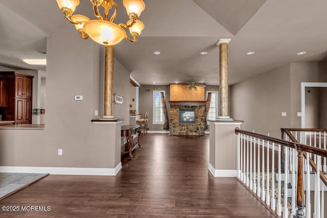 hallway featuring ornate columns, dark wood finished floors, baseboards, and an inviting chandelier