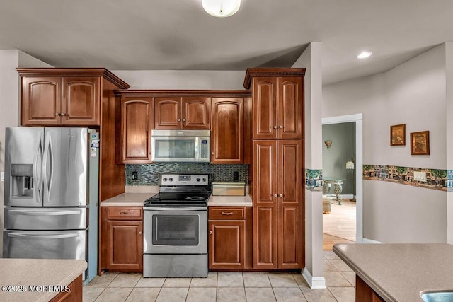 kitchen featuring baseboards, light countertops, light tile patterned floors, backsplash, and stainless steel appliances
