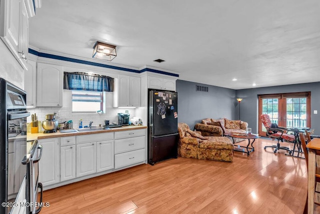 kitchen featuring open floor plan, light wood-type flooring, white cabinets, backsplash, and black appliances