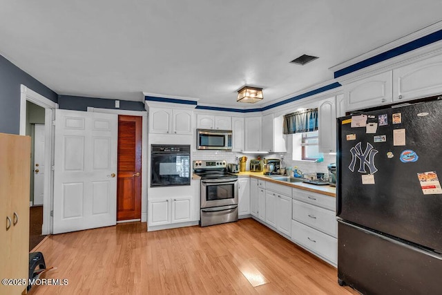 kitchen with light countertops, white cabinetry, light wood-style flooring, backsplash, and stainless steel appliances