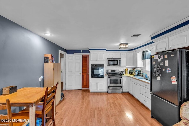 kitchen featuring visible vents, white cabinets, and black appliances