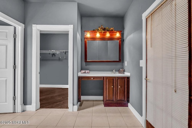 bathroom with baseboards, tile patterned floors, a spacious closet, and vanity