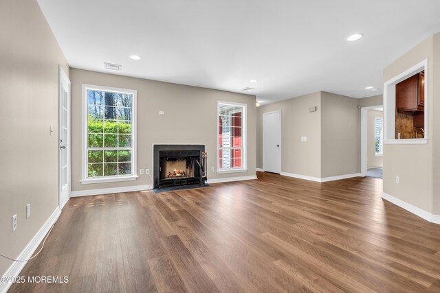 unfurnished living room with a fireplace with flush hearth, baseboards, wood finished floors, and visible vents