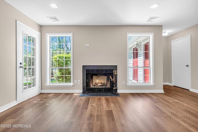unfurnished living room with a fireplace with flush hearth, wood finished floors, visible vents, and baseboards