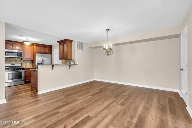 kitchen featuring stainless steel appliances, wood finished floors, visible vents, decorative backsplash, and a chandelier