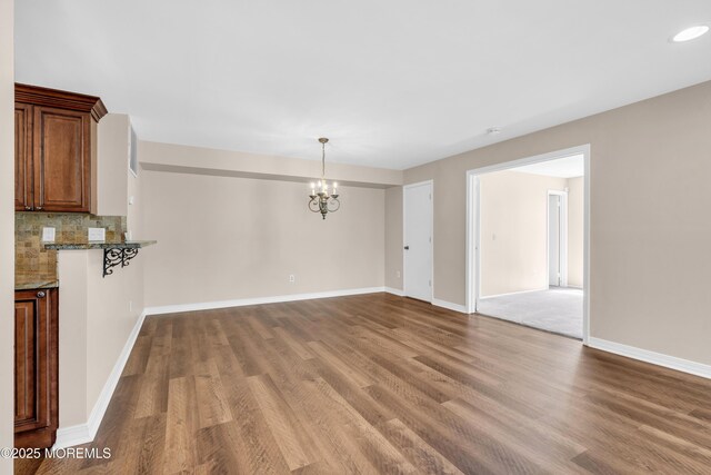 unfurnished dining area featuring baseboards, wood finished floors, recessed lighting, and a notable chandelier