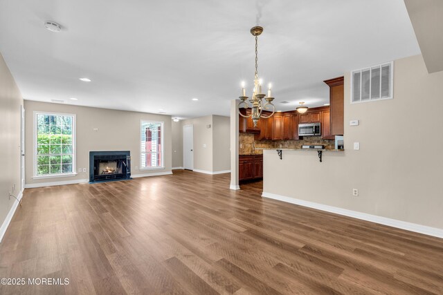 unfurnished living room with baseboards, wood finished floors, visible vents, and a notable chandelier