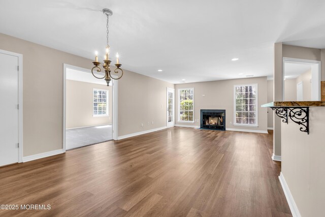 unfurnished living room featuring baseboards, a notable chandelier, and wood finished floors