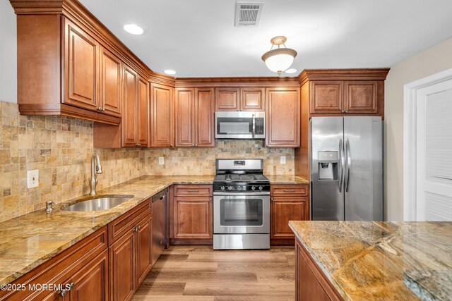 kitchen with a sink, light wood-style floors, light stone countertops, brown cabinetry, and appliances with stainless steel finishes