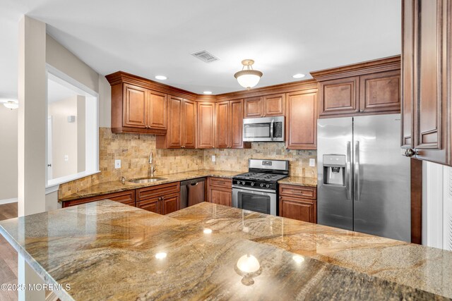 kitchen featuring stainless steel appliances, visible vents, a sink, decorative backsplash, and brown cabinetry