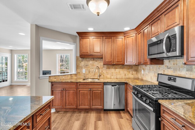 kitchen with stainless steel appliances, visible vents, a sink, light wood-type flooring, and brown cabinetry