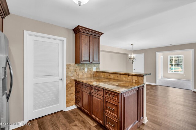 kitchen with light stone counters, stainless steel fridge with ice dispenser, backsplash, a peninsula, and dark wood-style flooring