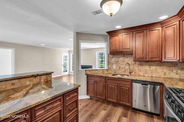 kitchen featuring stainless steel appliances, a sink, tasteful backsplash, wood finished floors, and light stone countertops