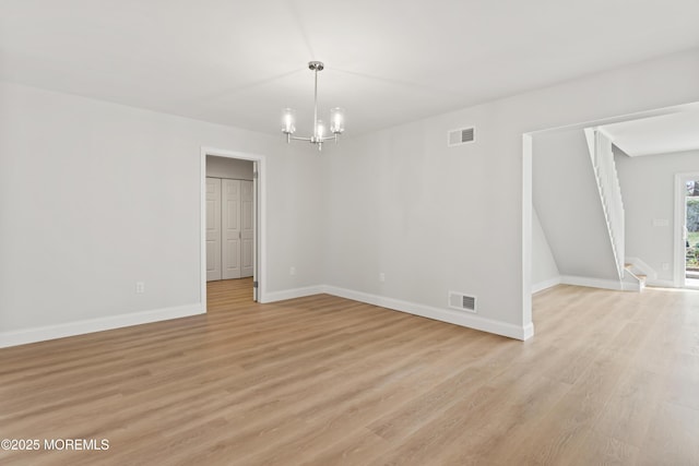 spare room featuring a notable chandelier, visible vents, baseboards, and light wood-type flooring