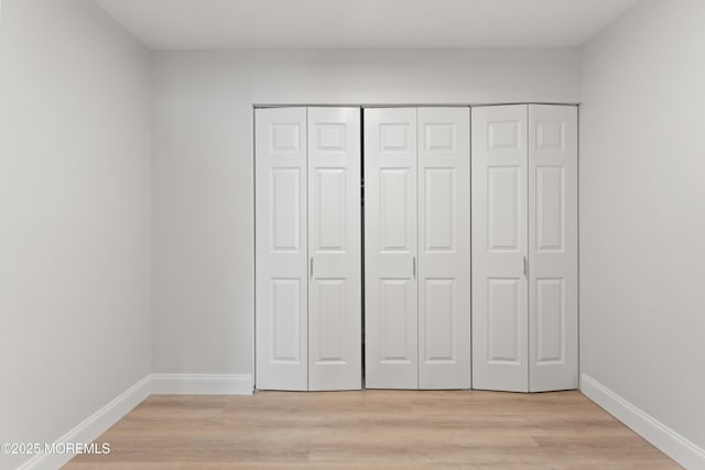 unfurnished bedroom featuring baseboards, light wood-type flooring, and a closet