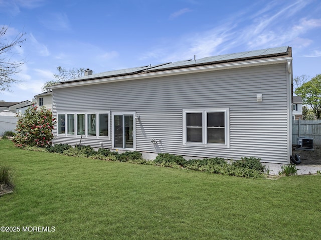 rear view of property featuring cooling unit, a yard, roof mounted solar panels, and a chimney