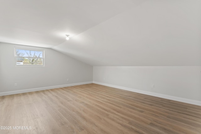 additional living space featuring baseboards, light wood-type flooring, and vaulted ceiling