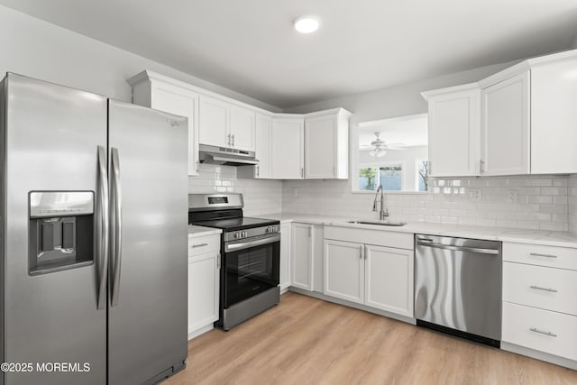 kitchen with stainless steel appliances, light wood-style floors, under cabinet range hood, white cabinets, and a sink