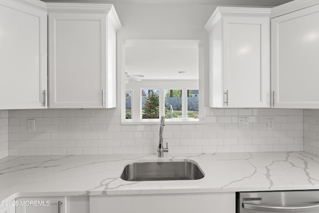 kitchen featuring white cabinetry, tasteful backsplash, stainless steel dishwasher, a sink, and light stone countertops