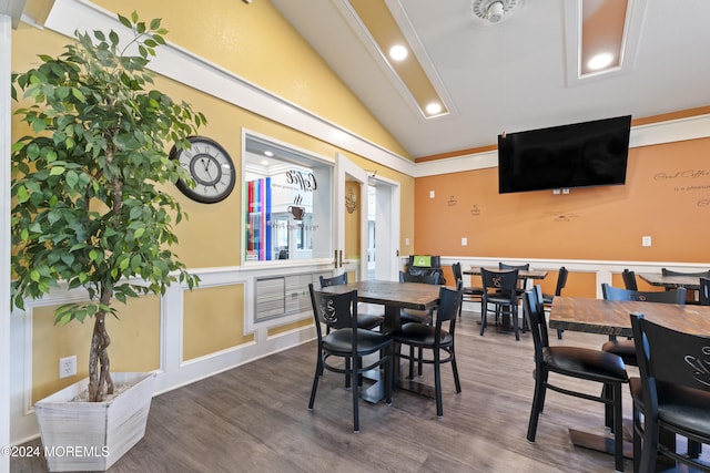 dining space with vaulted ceiling, wood finished floors, recessed lighting, and a wainscoted wall