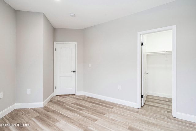unfurnished bedroom featuring light wood-style floors, baseboards, a spacious closet, and a closet