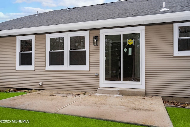 view of exterior entry featuring roof with shingles and a patio area