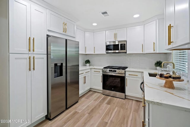 kitchen with light stone counters, a sink, light wood finished floors, stainless steel appliances, and white cabinetry