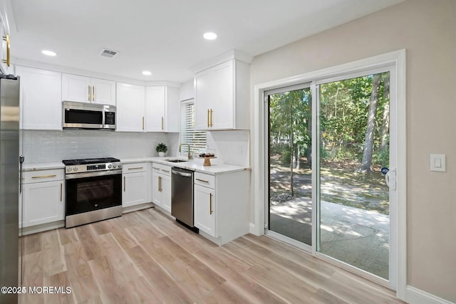 kitchen with light wood-style floors, tasteful backsplash, stainless steel appliances, and white cabinetry