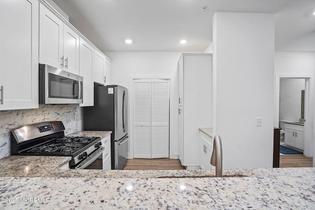 kitchen with stainless steel appliances, a sink, light wood-style flooring, and light stone counters