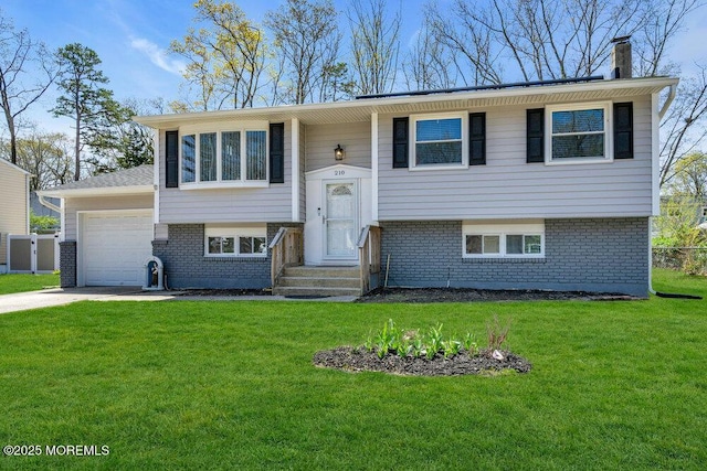 split foyer home with driveway, a chimney, a front yard, brick siding, and a garage