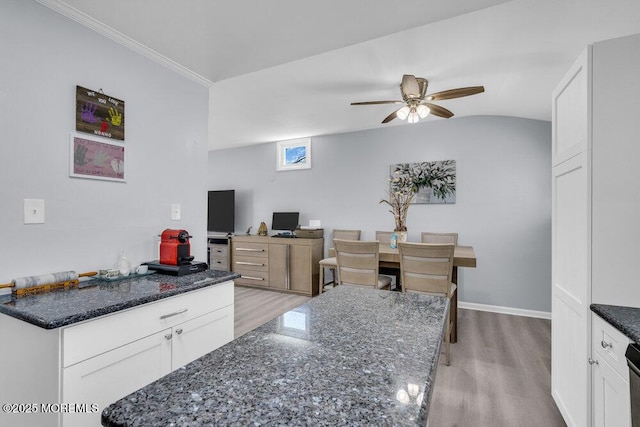 kitchen featuring dark stone countertops, ceiling fan, white cabinetry, and light wood-style floors