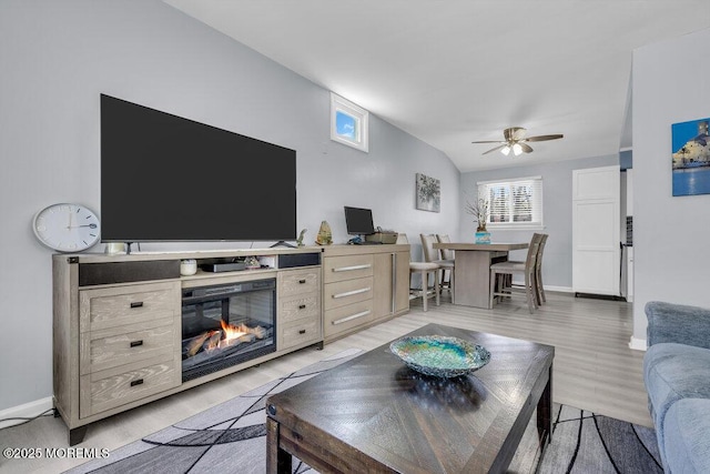 living area with baseboards, light wood-type flooring, ceiling fan, and a glass covered fireplace