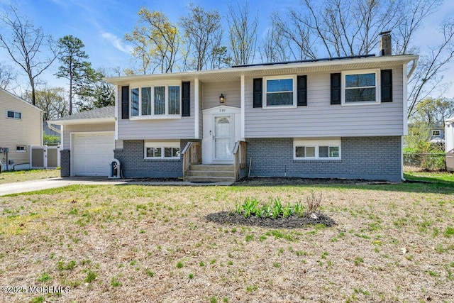 raised ranch with brick siding, a front lawn, concrete driveway, and an attached garage