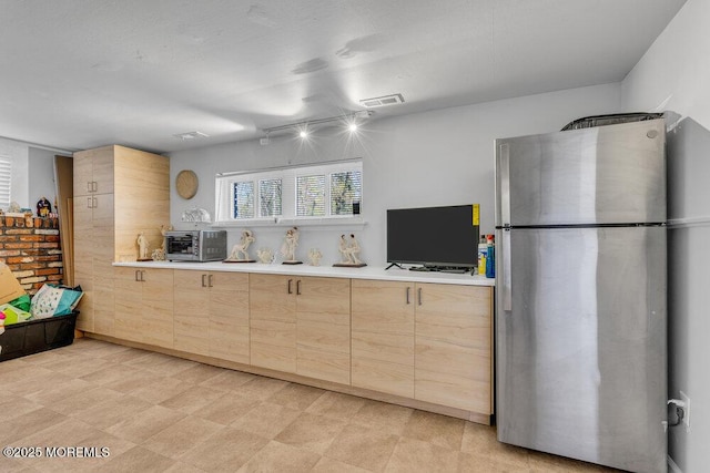kitchen featuring light brown cabinets, visible vents, light countertops, a toaster, and freestanding refrigerator