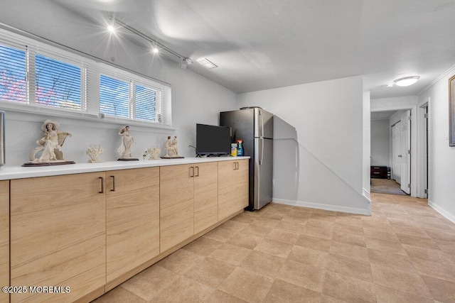kitchen featuring light brown cabinetry, baseboards, freestanding refrigerator, and light countertops