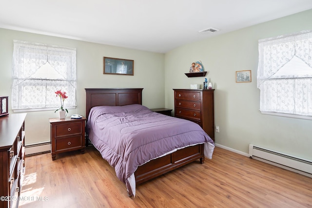 bedroom with visible vents, light wood-type flooring, and a baseboard heating unit