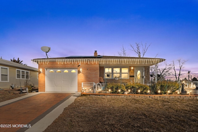 single story home featuring solar panels, a chimney, concrete driveway, brick siding, and an attached garage