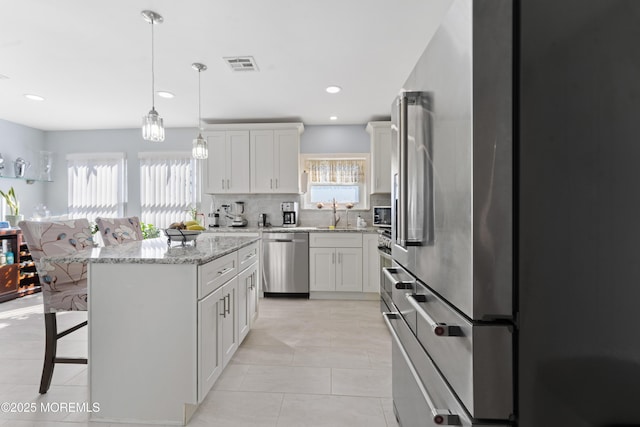 kitchen with a center island, visible vents, decorative backsplash, appliances with stainless steel finishes, and a breakfast bar area