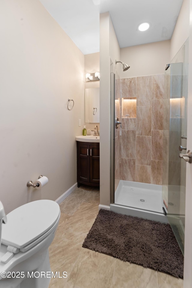 bathroom with baseboards, toilet, vanity, and tiled shower
