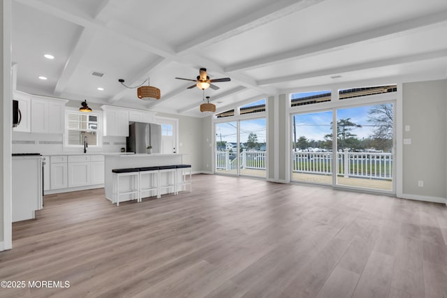 unfurnished living room featuring vaulted ceiling with beams, light wood-style flooring, a sink, baseboards, and a ceiling fan