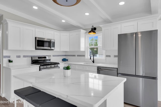 kitchen featuring a sink, a center island, backsplash, white cabinetry, and appliances with stainless steel finishes
