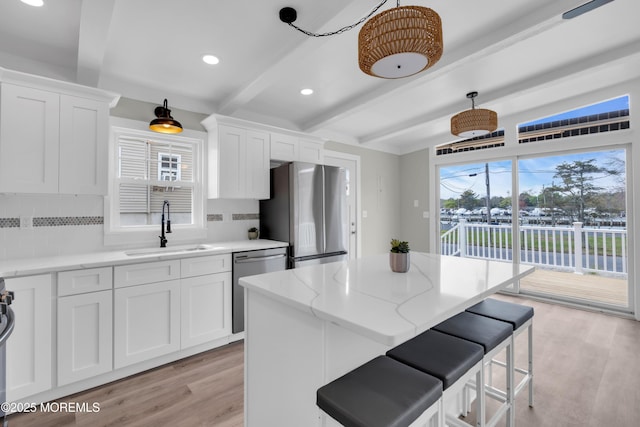 kitchen with a sink, beam ceiling, stainless steel appliances, light wood-type flooring, and tasteful backsplash
