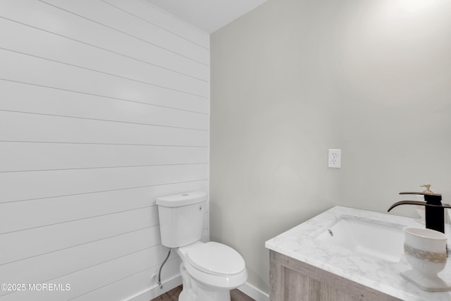 half bathroom featuring wood finished floors, vanity, toilet, and baseboards
