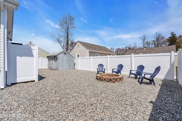 view of yard featuring a fire pit, a fenced backyard, a shed, and an outbuilding