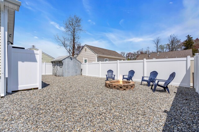 view of yard with an outbuilding, a storage shed, a fenced backyard, and an outdoor fire pit