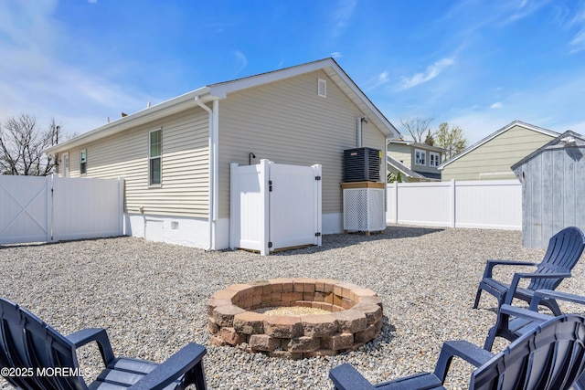 view of side of home with an outdoor structure, a gate, a storage shed, an outdoor fire pit, and a fenced backyard