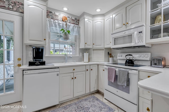kitchen with a sink, light tile patterned floors, white appliances, and white cabinetry